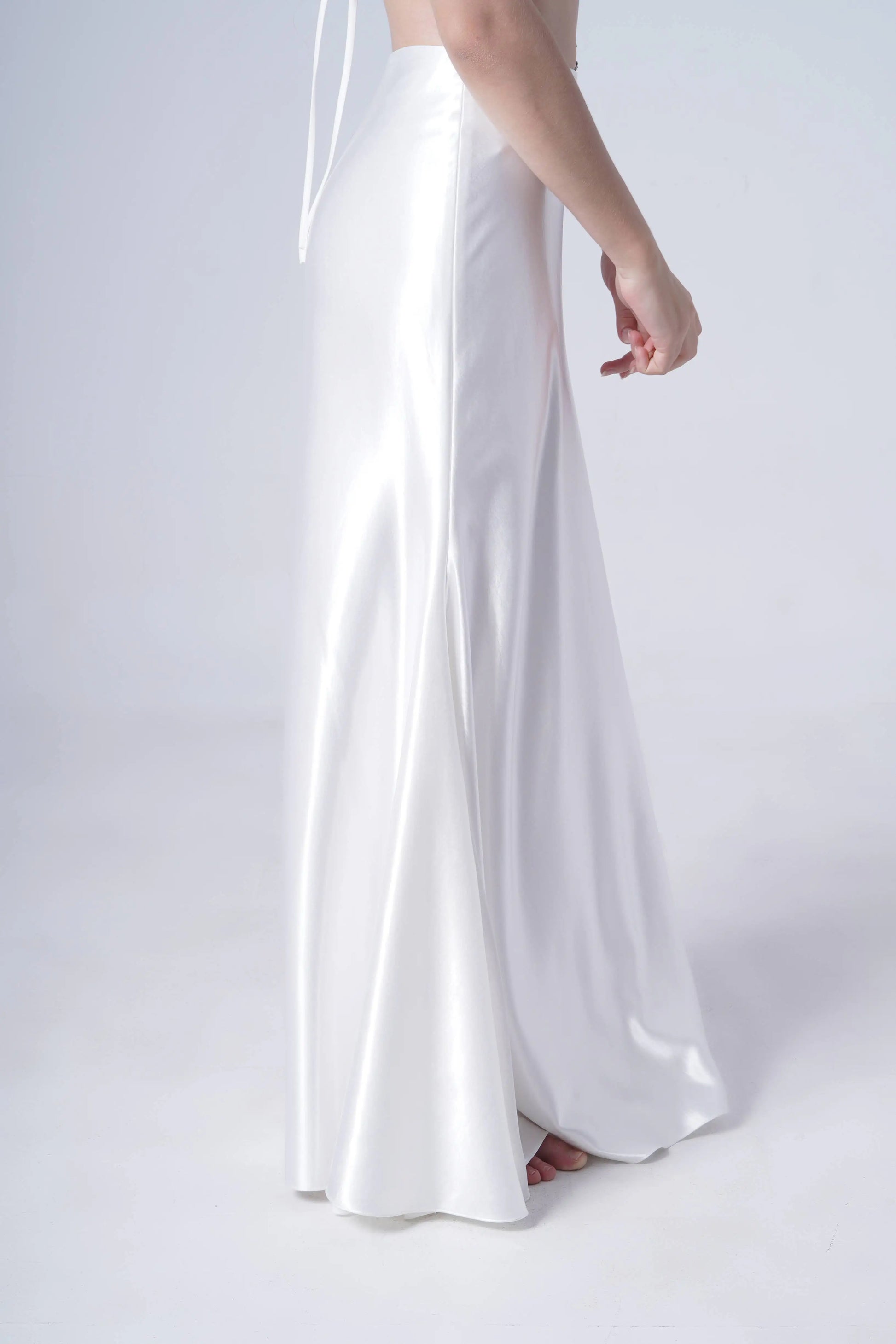 A person wears the TH&TH Topaz Bridal Skirt in Ivory Hammered Satin, standing on a white background with only their lower half visible, feet slightly showing and one arm relaxed by their side.