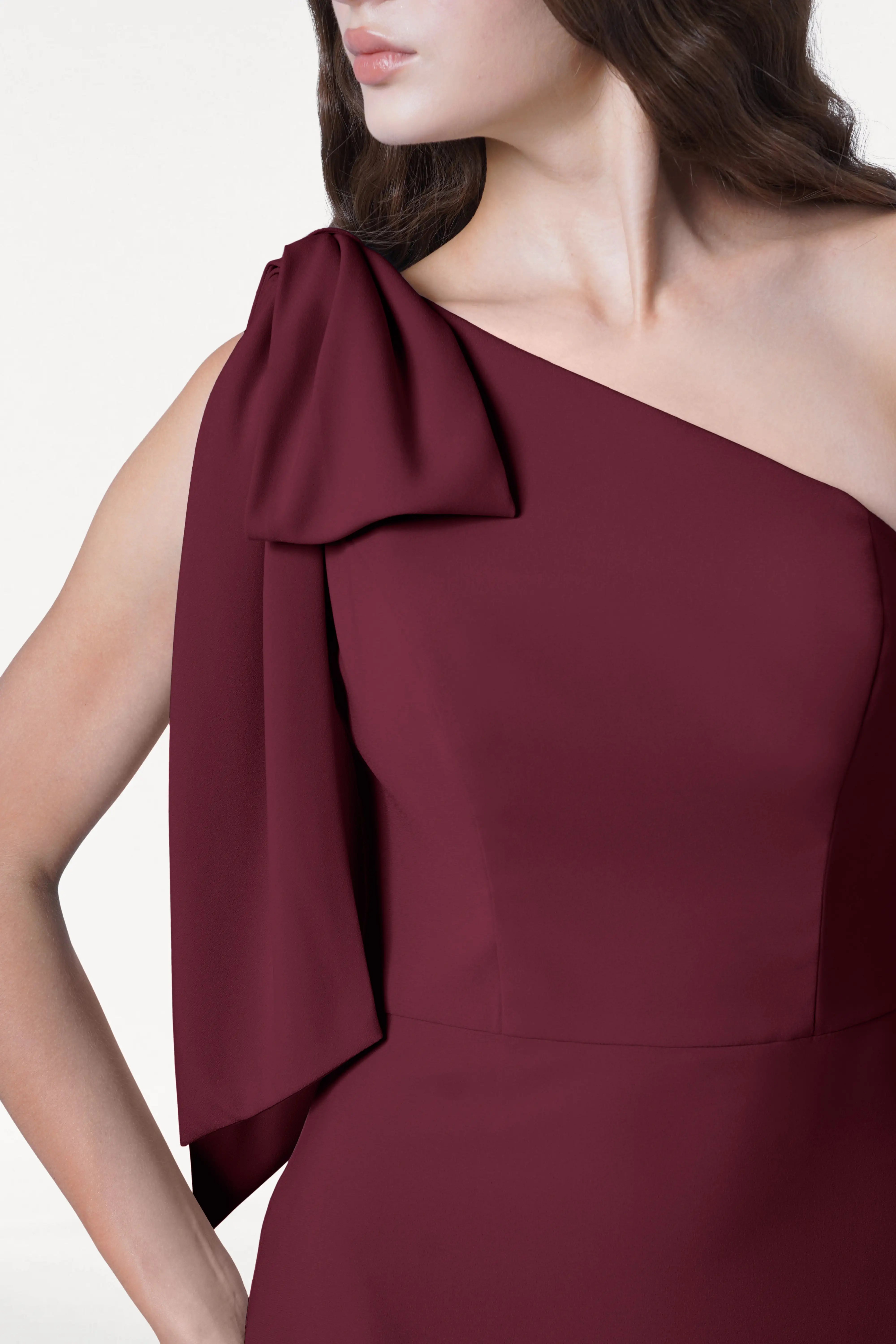 A woman wearing the TH&TH Valentina Bridesmaid Dress in Merlot— a modern, one-shoulder crepe gown with draped shoulder detail—shown from neck to waist.