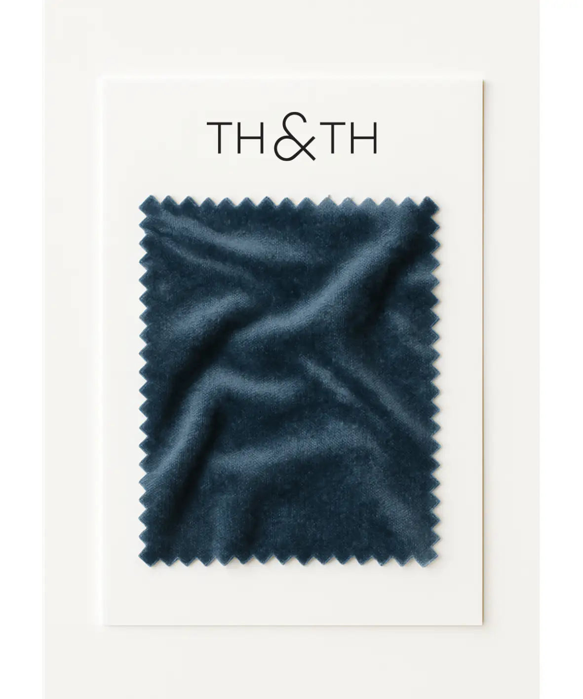 A rectangular swatch of dark blue stretch velvet fabric with zigzag edges is attached to a white card labeled TH & TH. The Velvet Swatch features a soft, slightly wrinkled texture and is perfect for bridesmaid dresses.