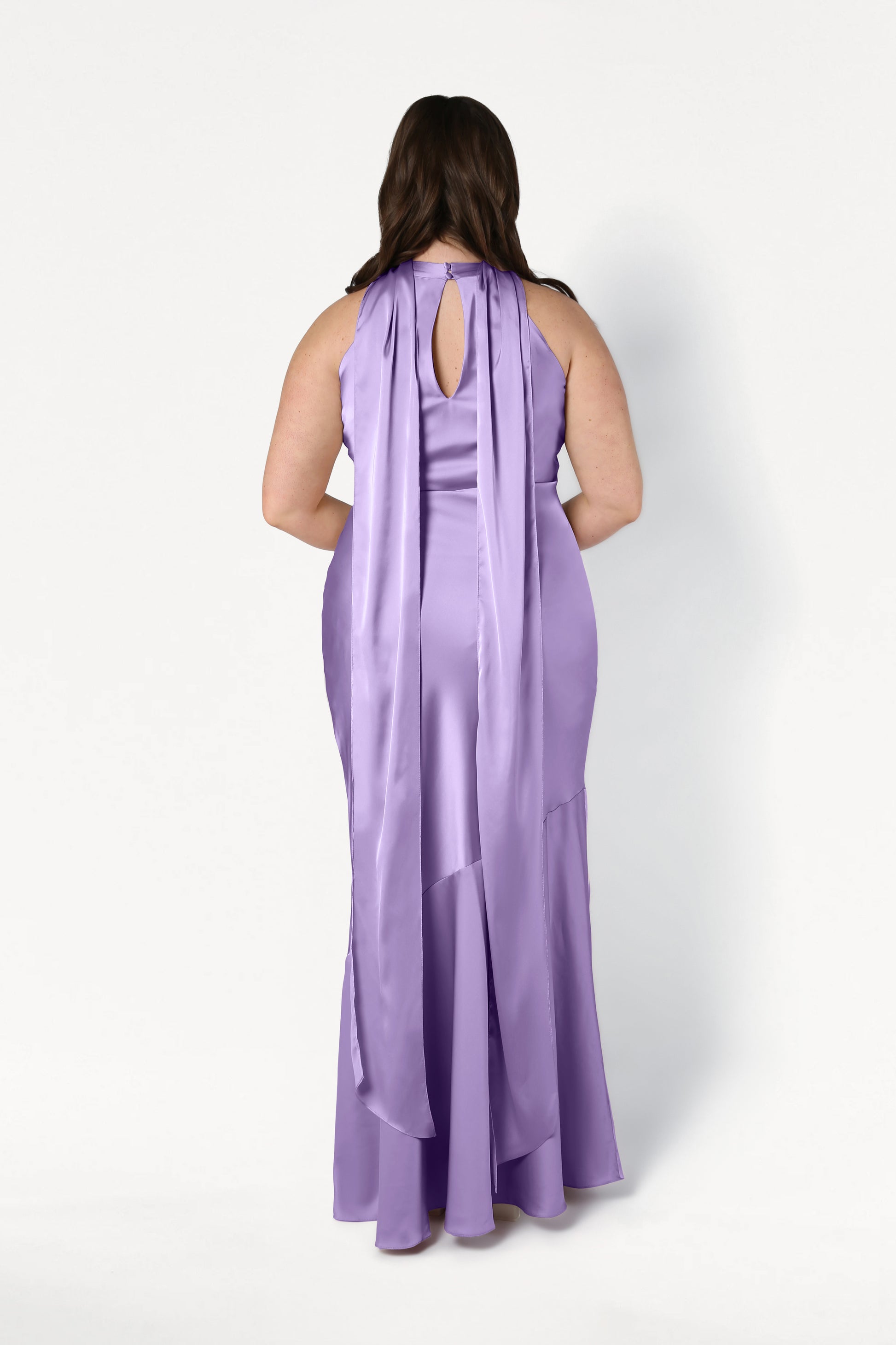 A woman, facing away from the camera against a white background, wears the TH&TH Mira Bridesmaid Dress in violet satin—a long, sleeveless gown with a keyhole cutout and two long sashes at the back.