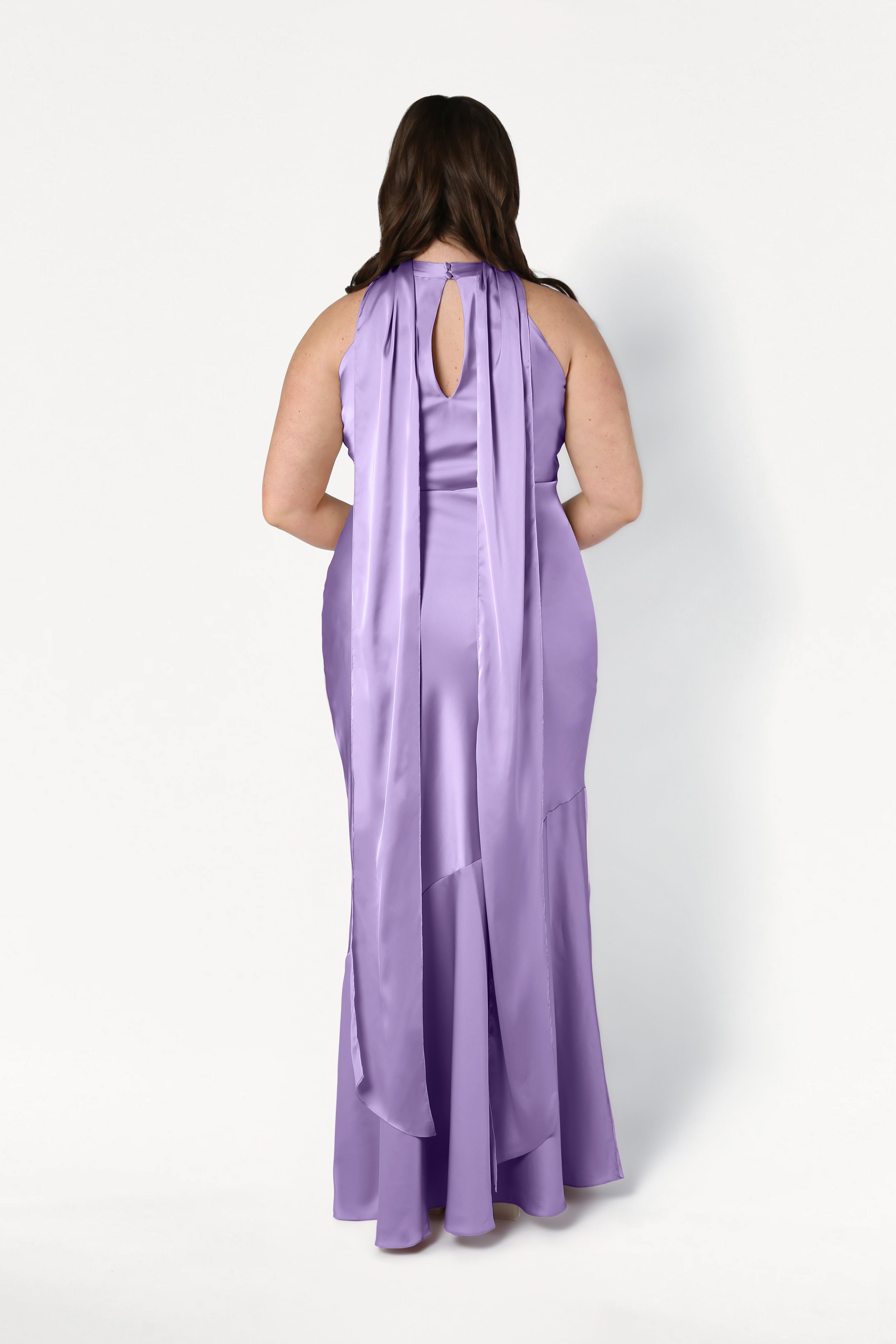A woman, facing away from the camera against a white background, wears the TH&TH Mira Bridesmaid Dress in violet satin—a long, sleeveless gown with a keyhole cutout and two long sashes at the back.