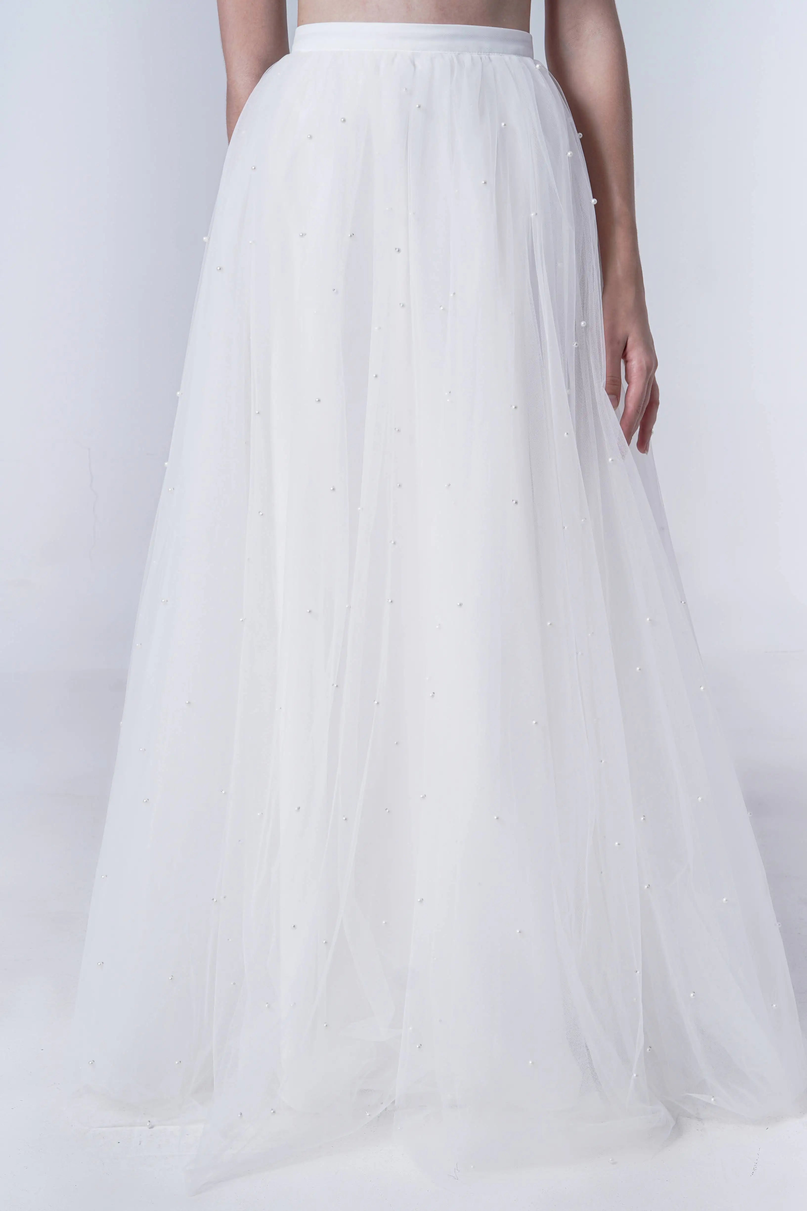 A person models the Wyatt Bridal Skirt in Ivory Tulle by TH&TH, a floor-length, slightly sheer tulle skirt with delicate pearl embellishments, adding an elegant touch to modern bridal separates against a plain white background.