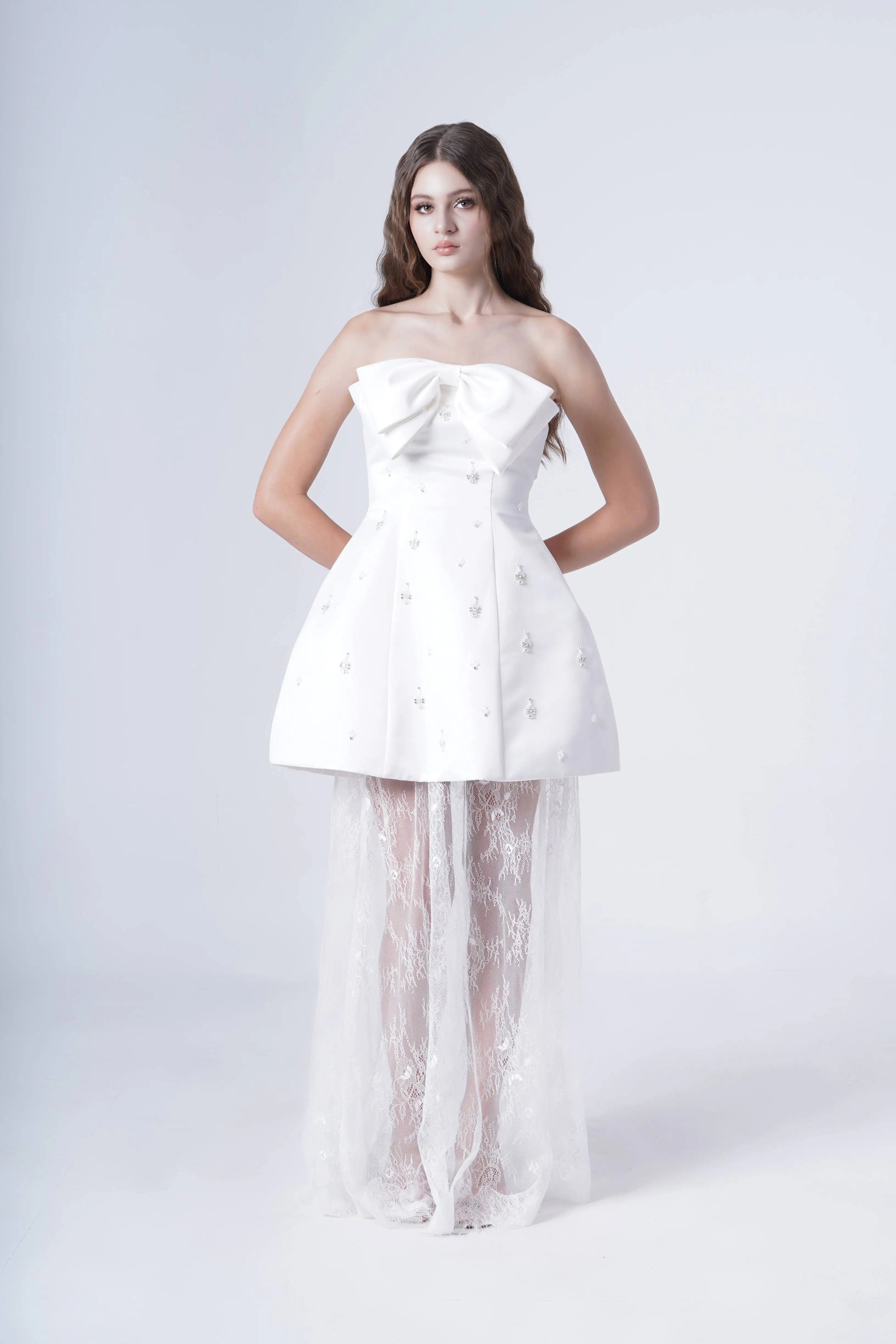 Woman wearing a strapless white dress with sheer overlay on a white background