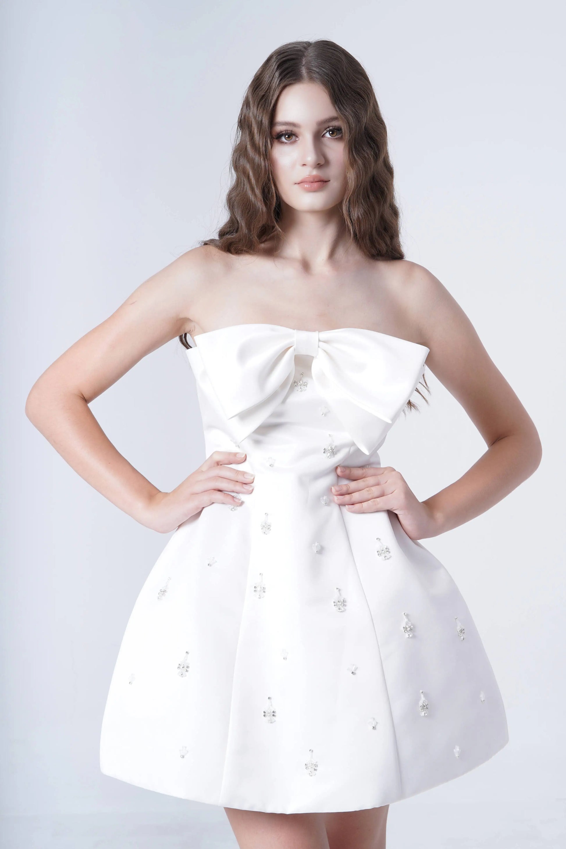 Woman wearing a white strapless dress with pearl embellishments on a light gray background