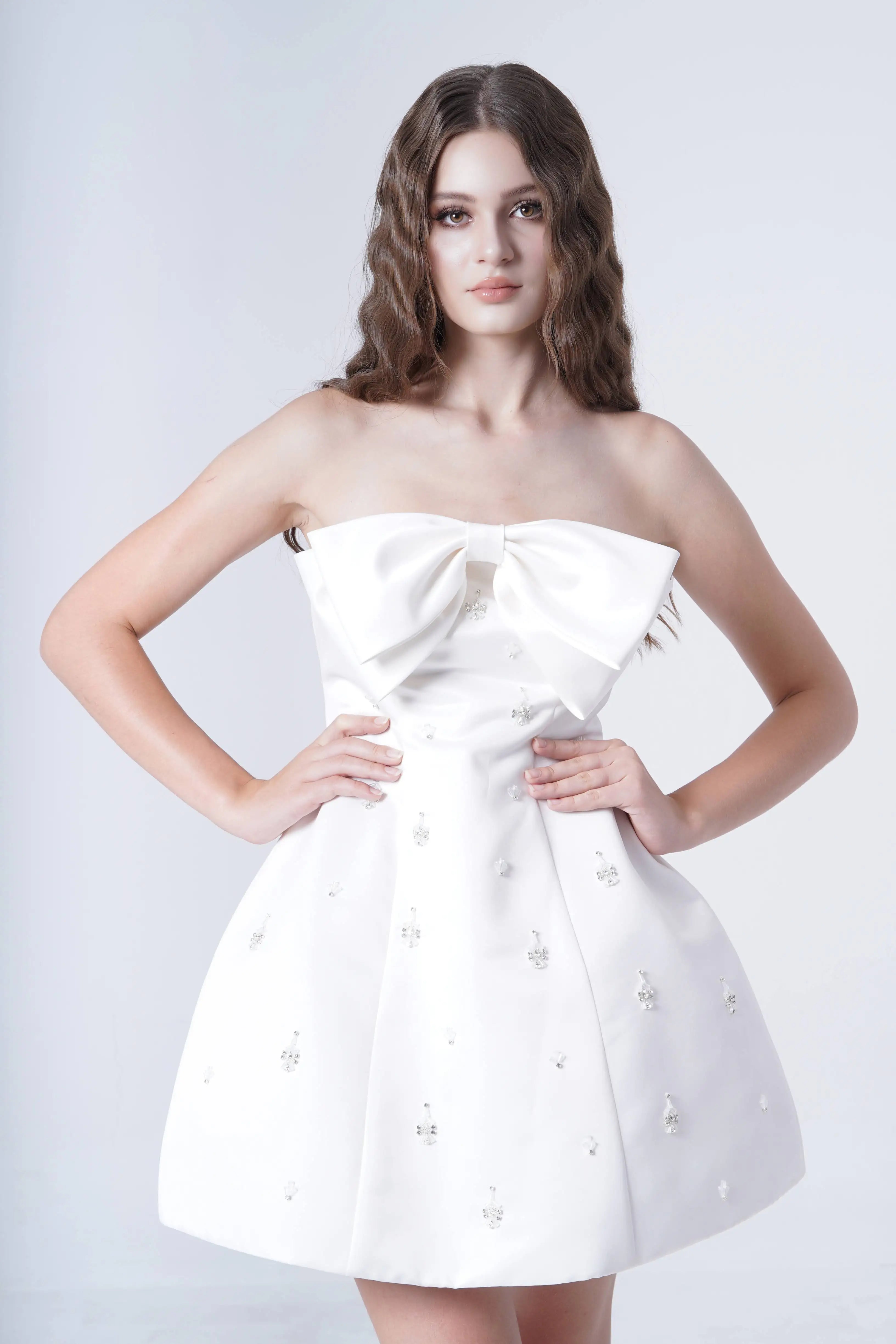 Woman wearing a white strapless dress with pearl embellishments on a light gray background