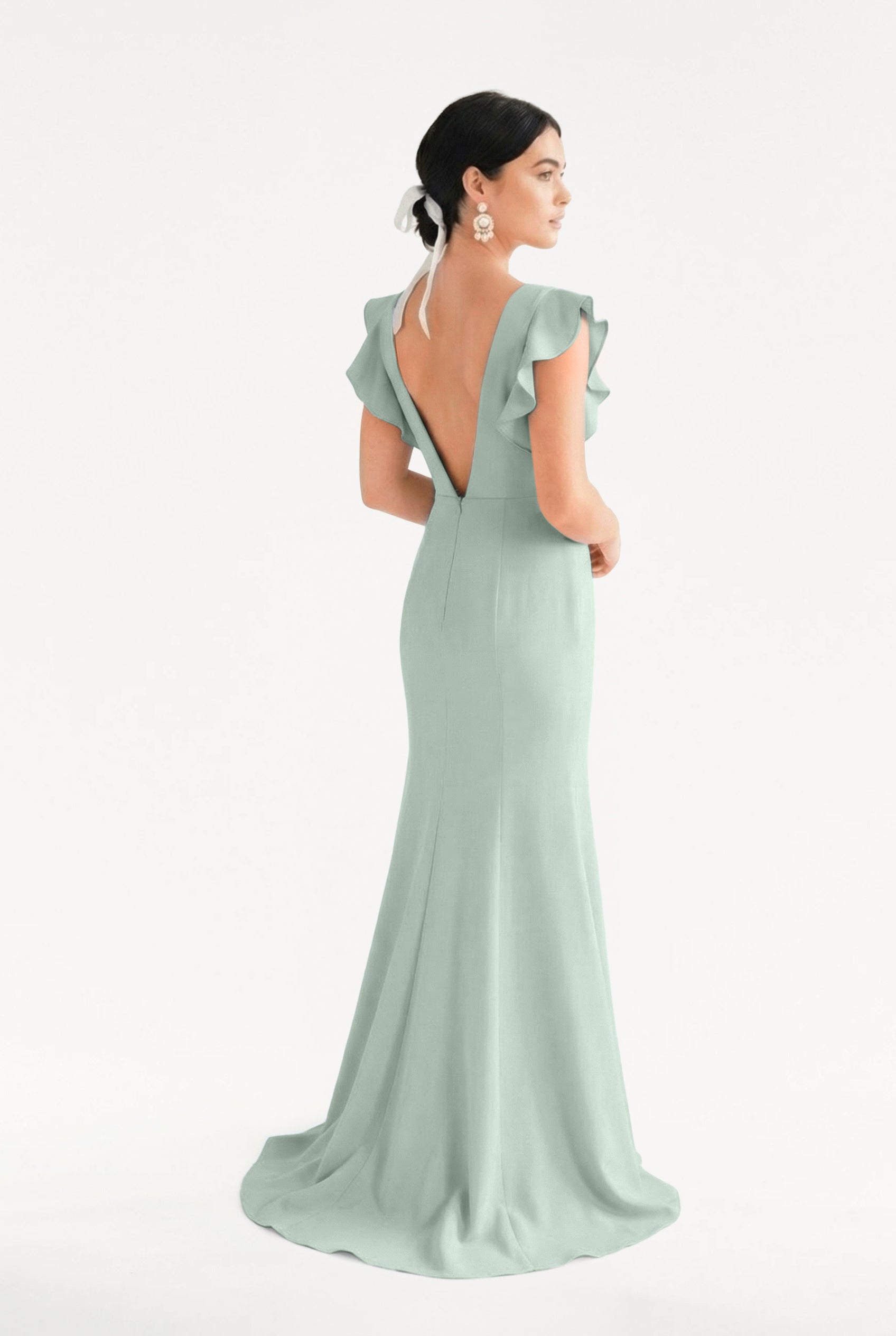 A woman wears the TH&TH Cecelia Moss Crepe Bridesmaid Dress in Sage Green, featuring flutter sleeves and a deep V-back, posing against a plain white background.