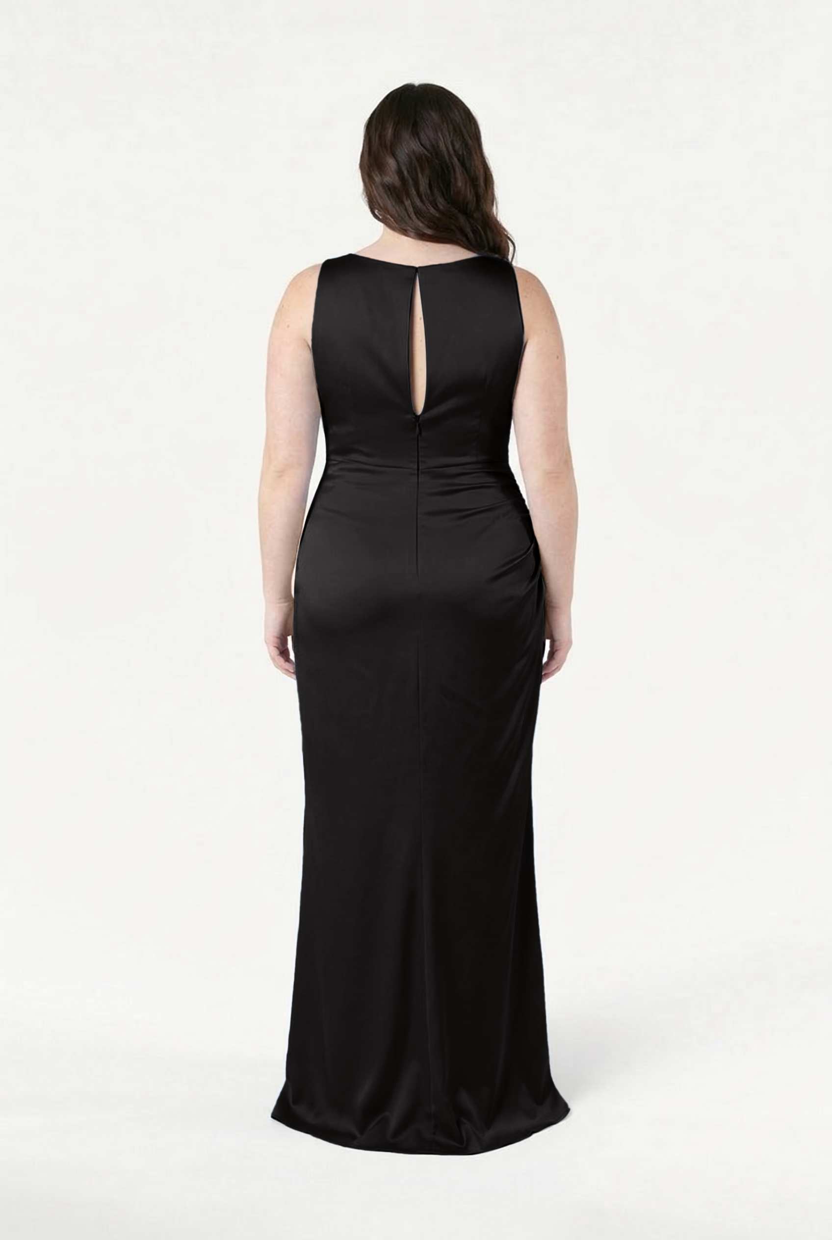 A woman with long dark hair models the TH&TH Nala Bridesmaid Dress in Black Satin, a sleeveless, floor-length gown with a keyhole back detail. She stands with her back to the camera against a plain white background.