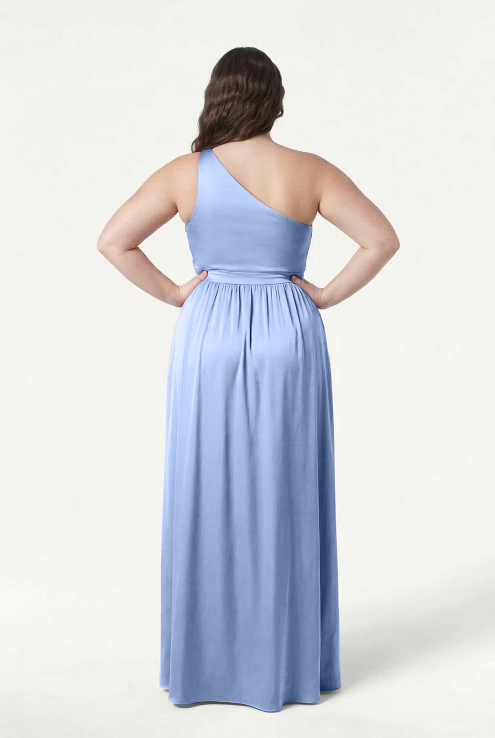 A woman stands with her back to the camera in the TH&TH Greta Bridesmaid Dress in Dusty Blue Satin, featuring a long, one-shoulder design with Grecian draping, a gathered waist, and flowing skirt for an elegant silhouette against a plain background.